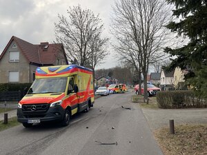 Bild vergr&ouml;&szlig;ern: Im Vordergrund ist ein Rettungswagen in der Tucholskystraße sehen. Weiter hinten steht der verunfallte weiße PKW, ein Mannschaftswagen der Feuerwehr Hennigsdorf und ein weiterer Notrufwagen.